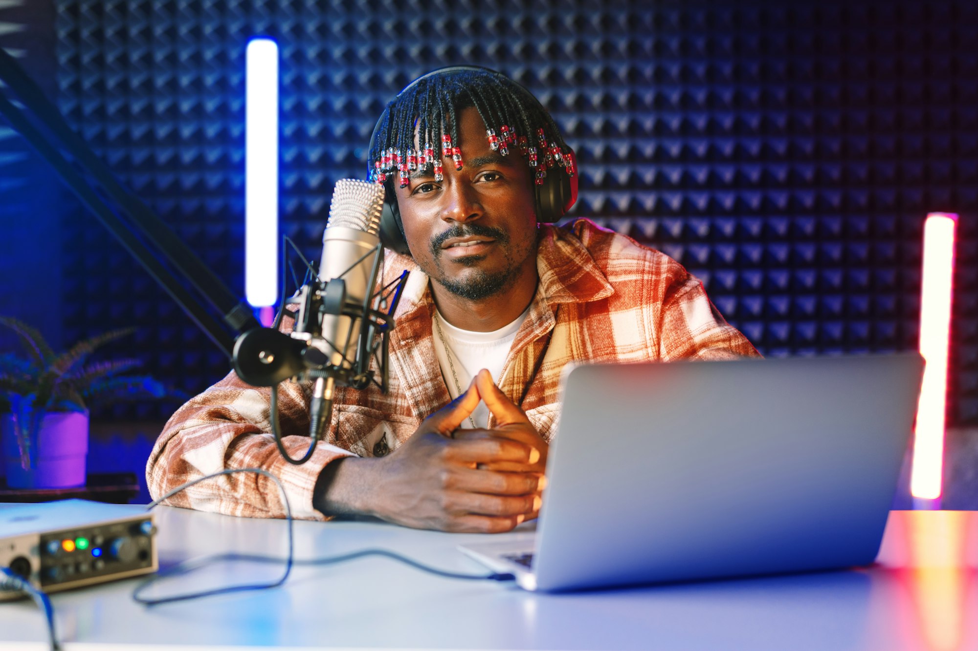 African radio host sitting at desk recording in studio with microphone and laptop